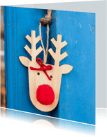 Kerstkaart met een houten rendier op een blauwe deur