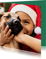 Kerstkaart met een kind met een kerstmuts en een hondje aait