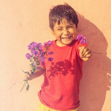 Wenskaart met lachend jongetje die paarse bloemen vasthoudt