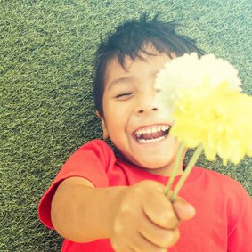 Wenskaart met een lachend kind die twee bloemen vasthoudt