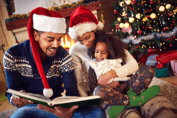 Vader, moeder en kind voor kerstboom lezen een boek