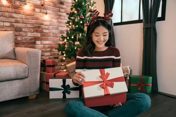 vrouw zit voor kerstboom met kerstcadeaus