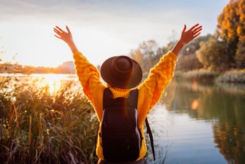 Vrouw met handen in de lucht kijkt naar zonsopkomst