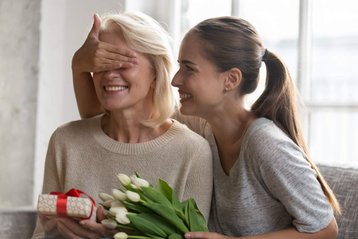 vrouw houdt hand voor ogen andere vrouw en geeft cadeau