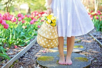 Meisje in wit jurkje houdt een mandje vol gele tulpen vast