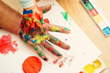 Kinderhand in vaderhand met vingerverf