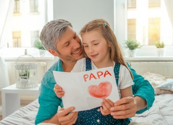 Vader met dochter op schoot bekijkt zelfgemaakt vaderdagkaart