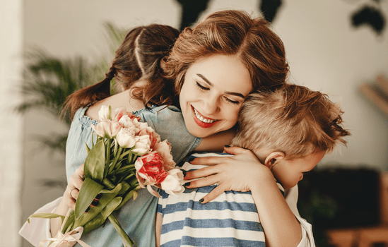 Moeder knuffelt zoon en dochter na ontvangen bloemen als moederdagcadeau