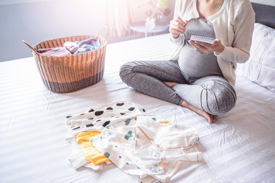 Zwanger vrouw op bed maakt checklist voor vluchttas bevalling